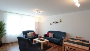 Un salon comprenant un canapé, deux fauteuils, une table basse et une table à manger en bois.