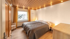 A bedroom with a wooden ceiling, a bed with a quilted blanket, a bedside table with a lamp, and a window with curtains. - Large Holiday Home near Winterberg with Garden, Terrace, & Garage (Winterberg)