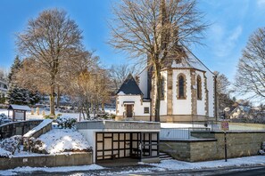 Une église dotée d’un clocher, d’un porche et de neige au sol.