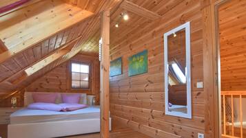 Een gezellig slaapkamer op zolder met een schuine kap, houten wanden, een bed met roze beddengoed en een raam.