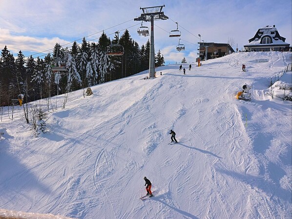 Une piste de ski avec un télésiège, des arbres et un bâtiment en arrière-plan.
