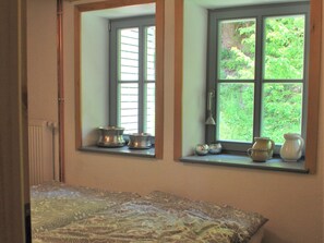 A bedroom with a bed, two windows with blinds, and a radiator.