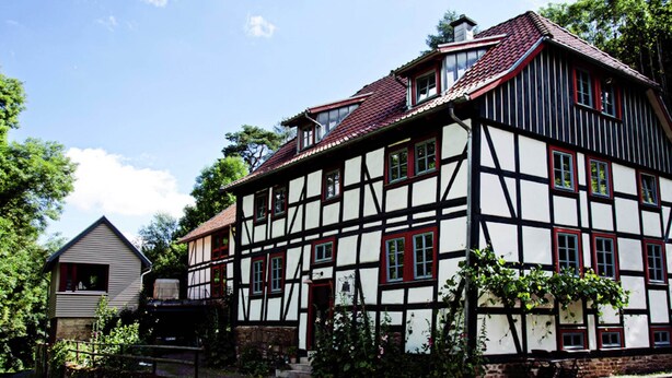 A traditional half-timbered house with a steeply pitched roof, multiple windows, and a small adjacent building. - Relaxing Watermill Hideaway (Heringen)
