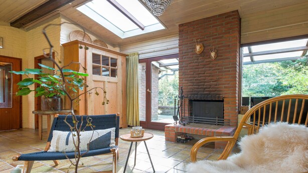 A cozy living room with a fireplace, wooden furniture, and a large window. - Holiday Home in Zorgvlied Near Drents (Zorgvlied)