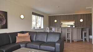 A modern living room with a dark leather sofa, a coffee table, and a kitchen area with a wooden countertop and bar stools. - Lovely Group House near Winterberg with Private Sauna, Garden, & Terrace (Hallenberg)