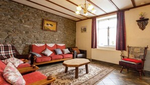 A cozy living room with a stone wall, a red sofa, a wooden coffee table, and a plaid armchair. - Holiday Home in Bastogne With Garden (Bastogne)