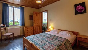 A bedroom with a wooden bed, a nightstand, a dresser, a chair, and a window with curtains. - Holiday Home in Bastogne With Garden (Bastogne)