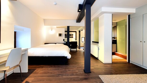 A modern bedroom with a large bed, a desk, and a chair. There is a wardrobe and a bathroom visible in the background. - Chic Mansion in Robertville (Waimes)