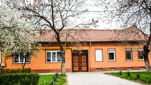 Un bâtiment à deux étages, doté d’un toit recouvert de tuiles rouges, d’une entrée centrale avec une double porte et d’un petit jardin à l’avant.