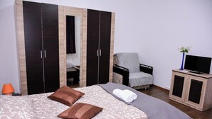 Une chambre à coucher avec un lit, des oreillers, une chaise, un téléviseur et une armoire.