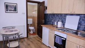 A compact kitchen with wooden cabinets, a gas stove, a dishwasher, and a small dining area with a table and chairs.