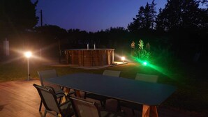Area patio esterna con tavolo e sedie, una struttura in legno e illuminazione decorativa.