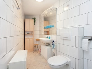A modern bathroom with white tiles, a sink, a toilet, and wooden cabinets. - Meadow View Cottage in Winterstein Thuringia near Ski Area (Waltershausen)