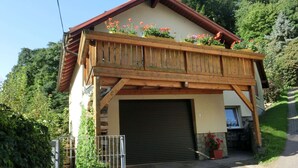 En tvåvåningsbyggnad med en träbalkong, ett garage och en trädgård med blommor.