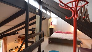 A bedroom with a sloped ceiling, a bed with pink pillows, a red coat rack, and a dining area with a table and chairs. - Holiday Home in Gemmenich With Forest Views (Plombieres)
