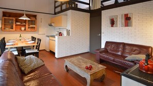 A cozy living room with a brown leather sofa, a wooden coffee table, and a dining area with a wooden table and chairs. - Holiday Home in Gemmenich With Forest Views (Plombieres)