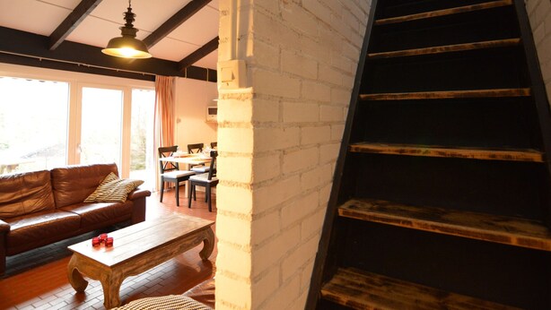 A living room with a brown leather sofa, wooden coffee table, and a staircase with wooden steps. - Holiday Home in Gemmenich With Forest Views (Plombieres)