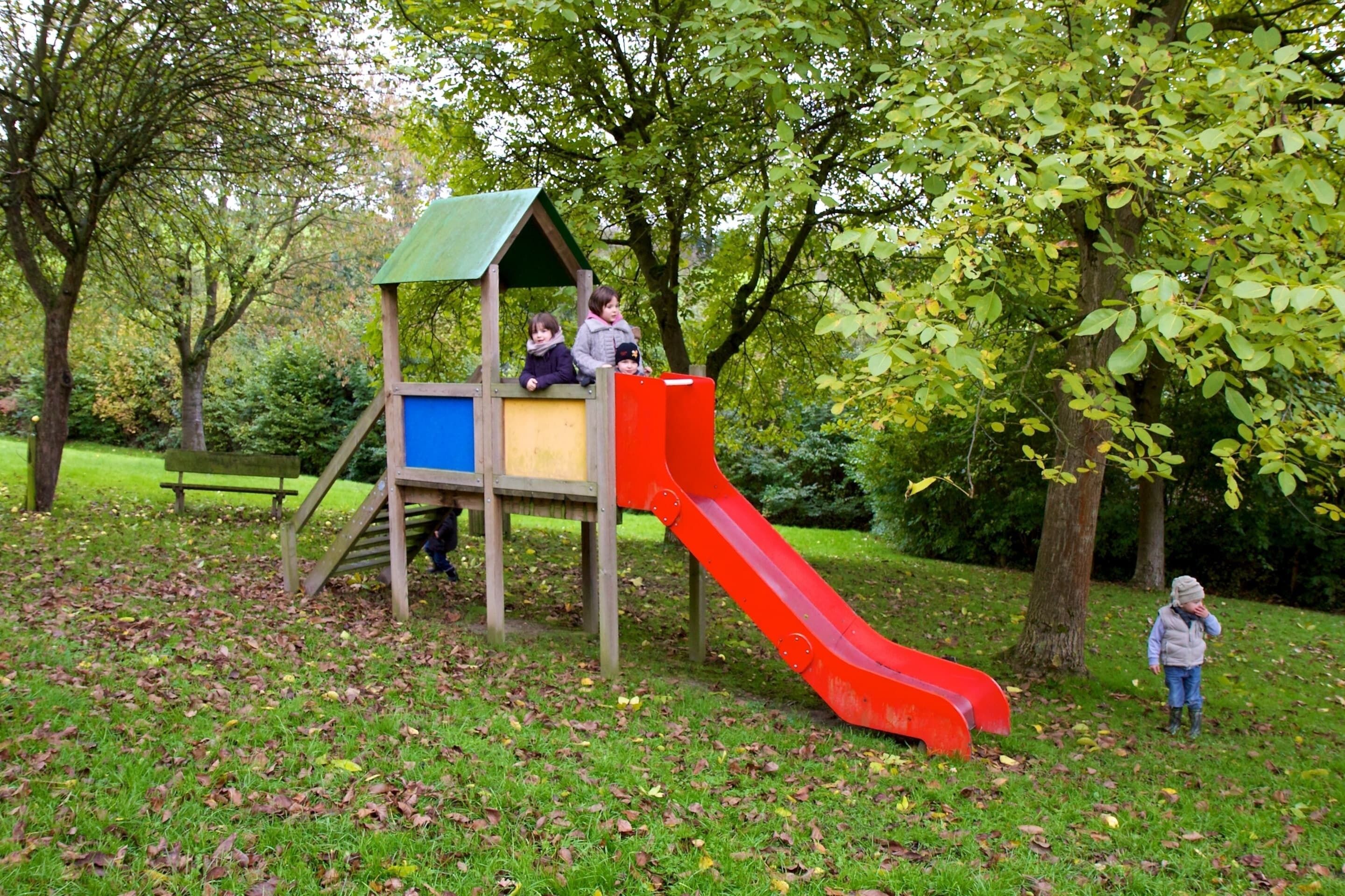A playground with a slide and climbing area, surrounded by trees and grass.