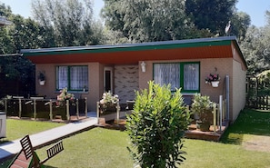 A small brick house with a green roof, two windows with green curtains, and a small garden with potted plants. - Cozy Apartment in Boltenhagen Germany near Beach (Boltenhagen)