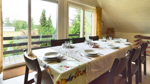 Un comedor con una mesa dispuesta para cuatro personas, ventanas amplias y vistas al exterior con vegetación.