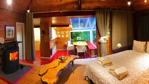 Ein gemütliches Holzhaus mit Kamin, Essbereich und einem Bett mit Handtüchern.