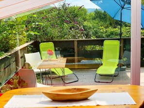 A wooden table with a bowl, two chairs, and a small table with a vase and glasses.