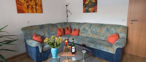 A living room with a blue patterned sofa, a glass coffee table, and a vase of flowers.