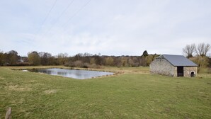 Un bâtiment en pierre, doté d’un toit en pente, situé près d’un étang dans un champ verdoyant.