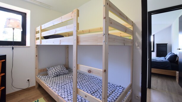 Un lit superposé avec un matelas à motifs, un bureau avec une lampe et une fenêtre avec des stores.