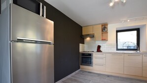 Une cuisine moderne dotée d’un réfrigérateur en acier inoxydable, de meubles en bois et d’une fenêtre laissant entrer la lumière naturelle.