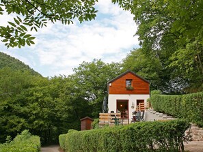 A two-story wooden cabin with a balcony, surrounded by lush greenery and a hillside. - Cottage With a Terrace and a View of the Valley (Aywaille)