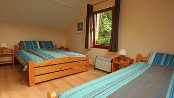 A bedroom with two wooden beds, a window with curtains, a radiator, and a framed picture on the wall.