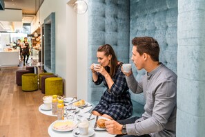 Una pareja desayunando en una mesa, en un interior moderno con pared acolchada y zona de estar.