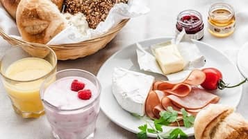 Ein Frühstücksbuffet mit Brot, Käse, Schinken und einem Glas Saft.