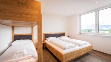 Une chambre avec deux lits, dont un lit superposé et l’autre un lit simple, tous deux dotés d’une structure en bois et de draps blancs.