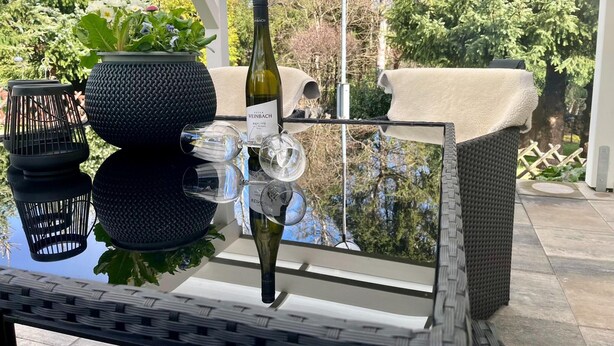A glass table with a bottle of wine, glasses, and a potted plant. - Apartment With Private Terrace (Harzgerode)
