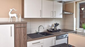 A modern kitchen with white cabinets, a black sink, and a stainless steel range hood. - Apartment With Private Terrace (Harzgerode)