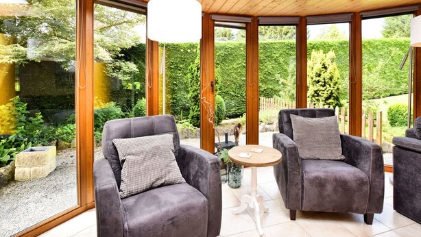 A sunroom with large windows, wooden ceiling, and two grey armchairs with cushions. - Beautiful Holiday Home in Durbuy With Garden (Durbuy)