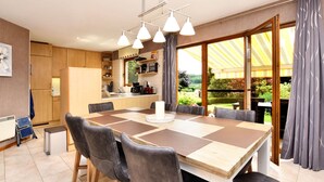 A modern kitchen with wooden cabinets, a dining area with a large table and chairs, and a view of a garden through large windows. - Beautiful Holiday Home in Durbuy With Garden (Durbuy)