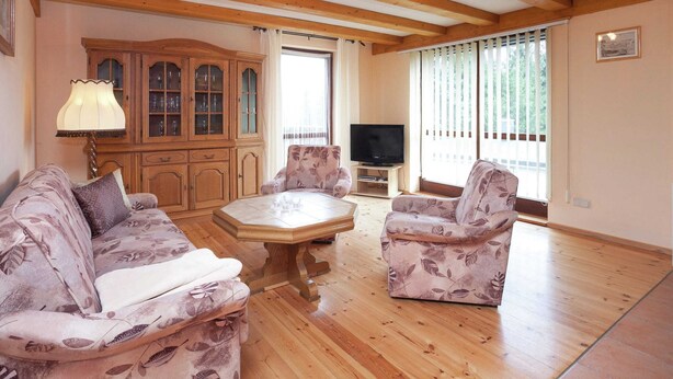 A living room with wooden floors, a wooden ceiling, a cabinet, a television, and two patterned sofas. - Quaint Holiday Home in Güntersberge near Lake (Harzgerode)
