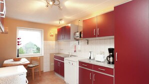 A compact kitchen with red cabinets, a white dishwasher, and a window with a view of greenery. - Quaint Holiday Home in Güntersberge near Lake (Harzgerode)