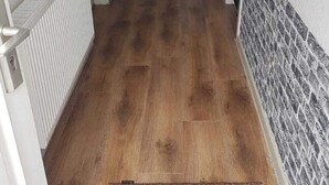Un couloir doté d’un plancher en bois, de murs blancs et d’un mur orné d’un motif sur le côté droit.