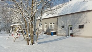 Un espace extérieur enneigé, avec une balançoire et un bâtiment doté de nombreuses fenêtres et portes.