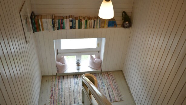Un escalier donnant sur une fenêtre, un luminaire suspendu et une bibliothèque remplie de livres.