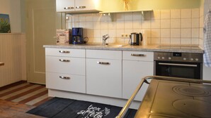 Une cuisine avec des meubles blancs, une machine à café, une bouilloire et une cuisinière.