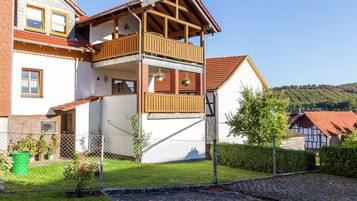 A two-story house with a balcony, a garden, and a cobblestone path.