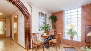 Una habitación amplia con chimenea de ladrillo, zona de comedor con sillas y mesa, y ventanas grandes que dejan entrar luz natural.