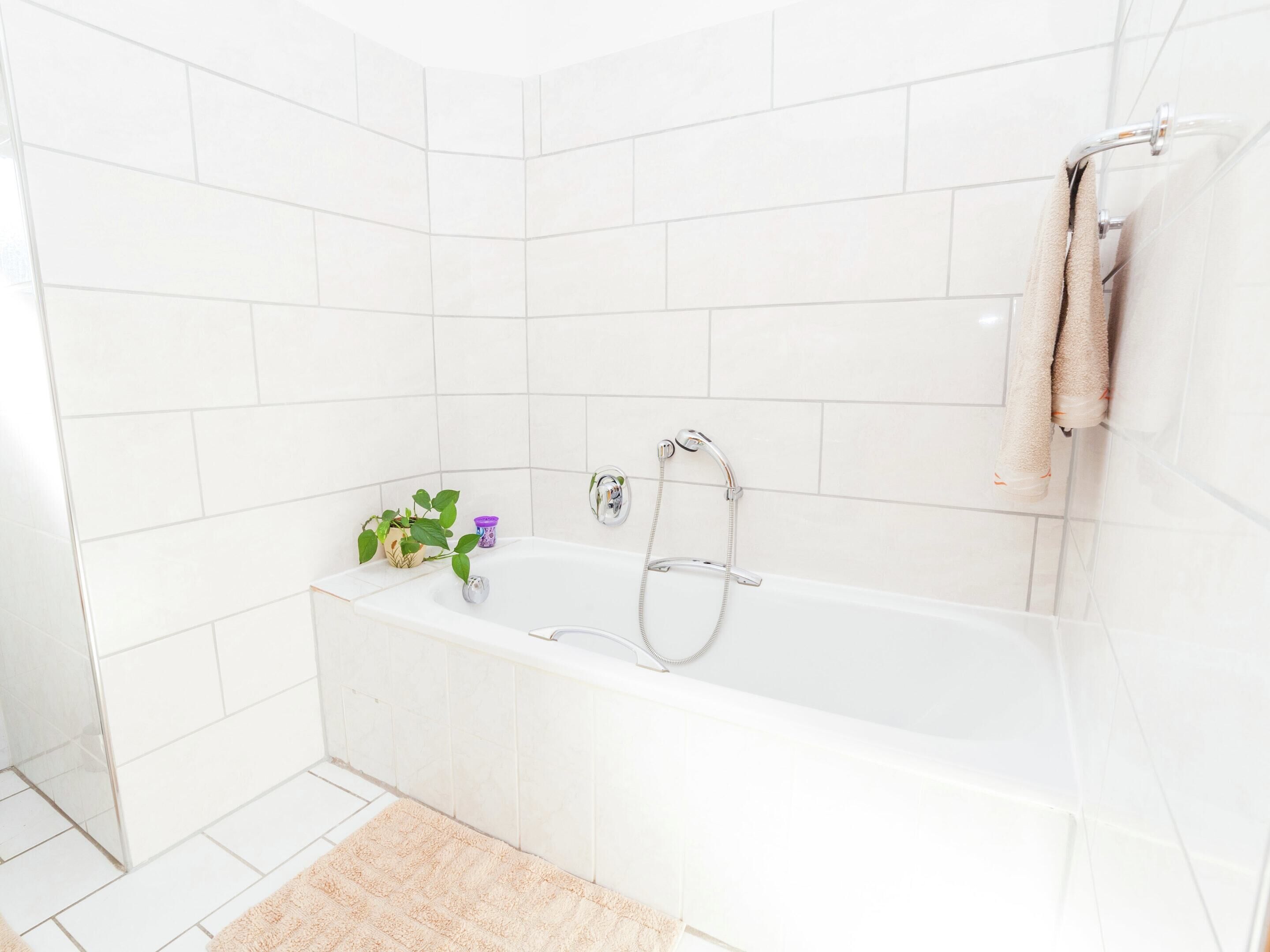 Ein modernes Badezimmer mit weißen Fliesen, einer Badewanne, einer Dusche, einem Handtuchhalter und einer kleinen Pflanze.