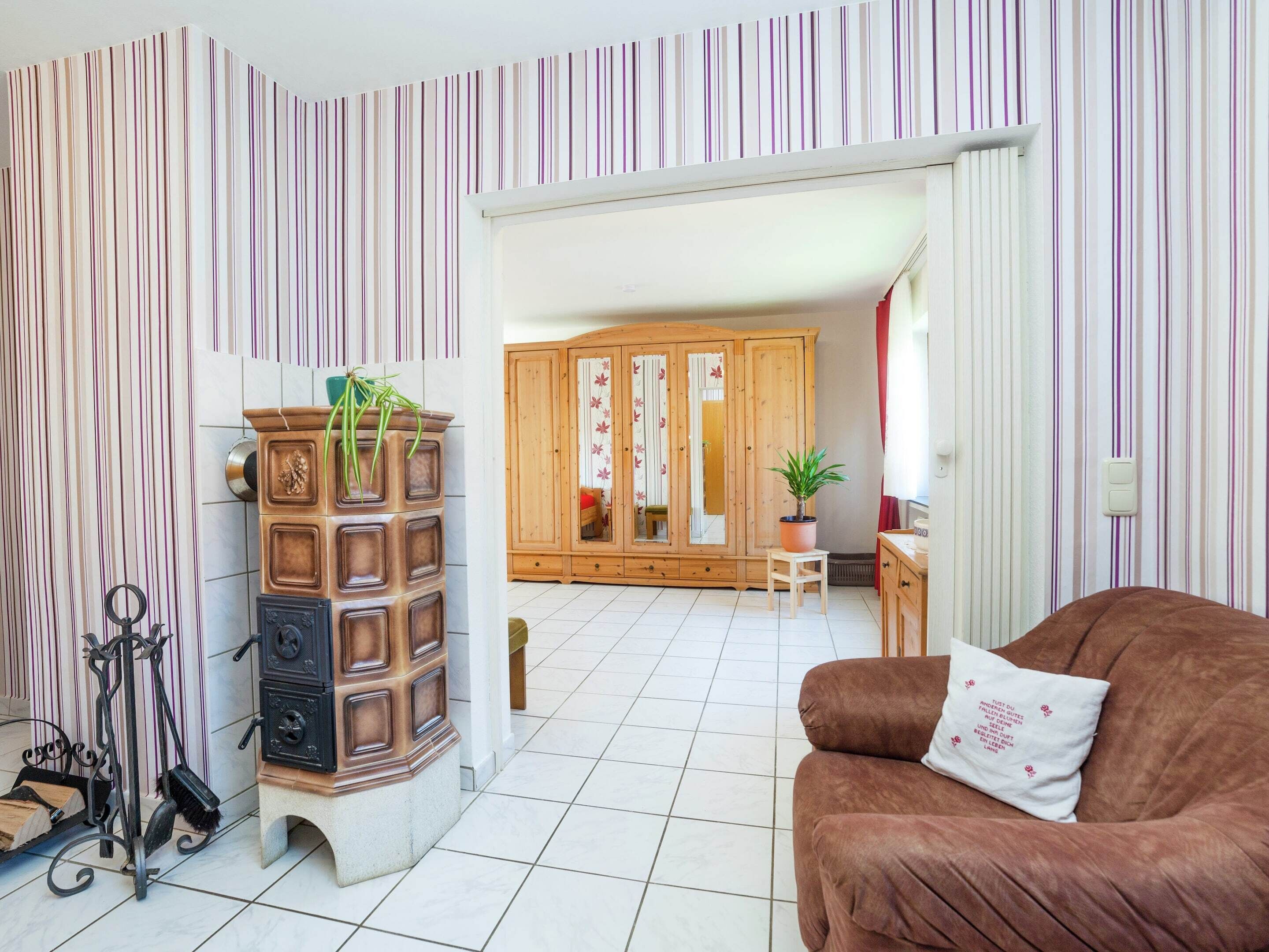 A living room with a brown sofa, a wooden cabinet with plants, and a tiled floor.