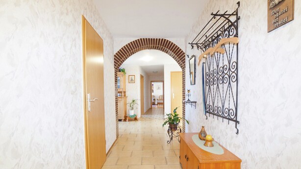 Un pasillo con puerta de madera, suelo de baldosas, un mueble de madera y una estantería metálica decorativa.